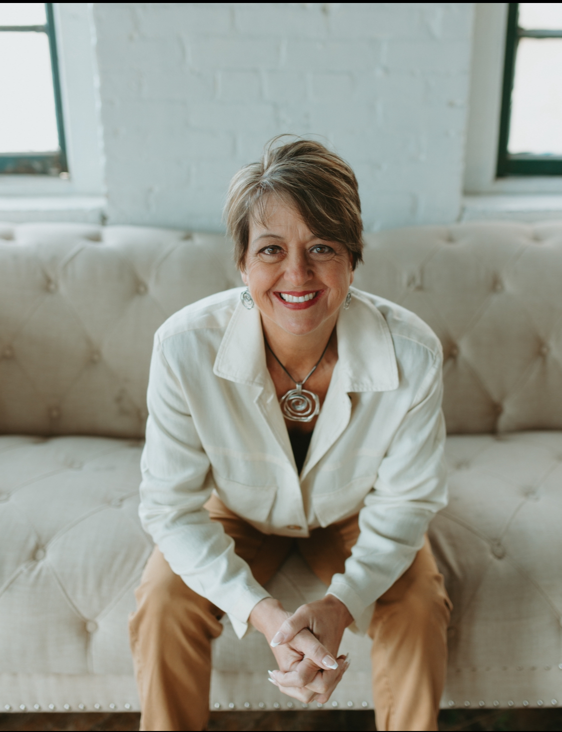 Heather sitting on a couch, smiling in a bright studio